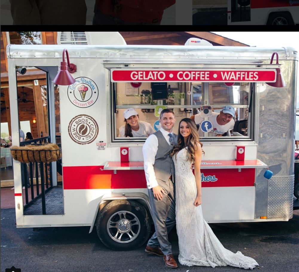 A couple in wedding attire poses in front of a red and white gelato, coffee, and waffles food trailer.