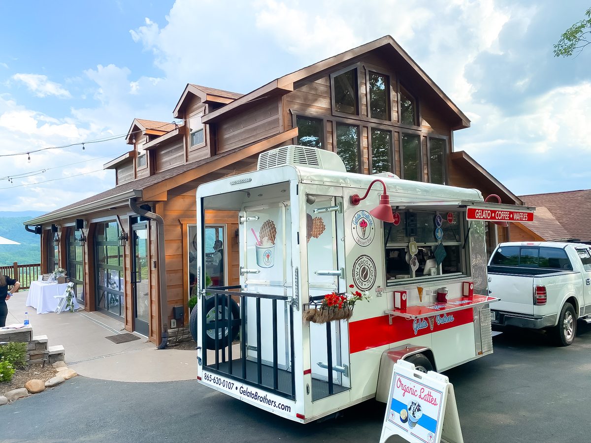 A red and white gelato cart sits parked in front of a wooden building under blue skies in East Tennessee.