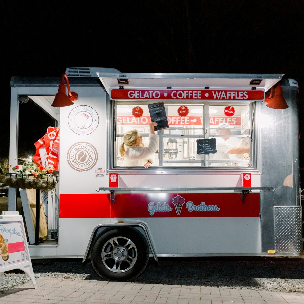 A red and white food trailer with "GELATO • COFFEE • WAFFLES" signage displayed at an outdoor event venue.