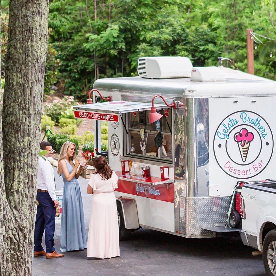 Couple and guest enjoy treats from a red and white catering trailer at an outdoor event.